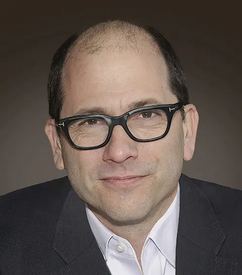 Headshot of author Patchen Barss, wearing dark-rimmed glasses, a white shirt and a dark jacket
